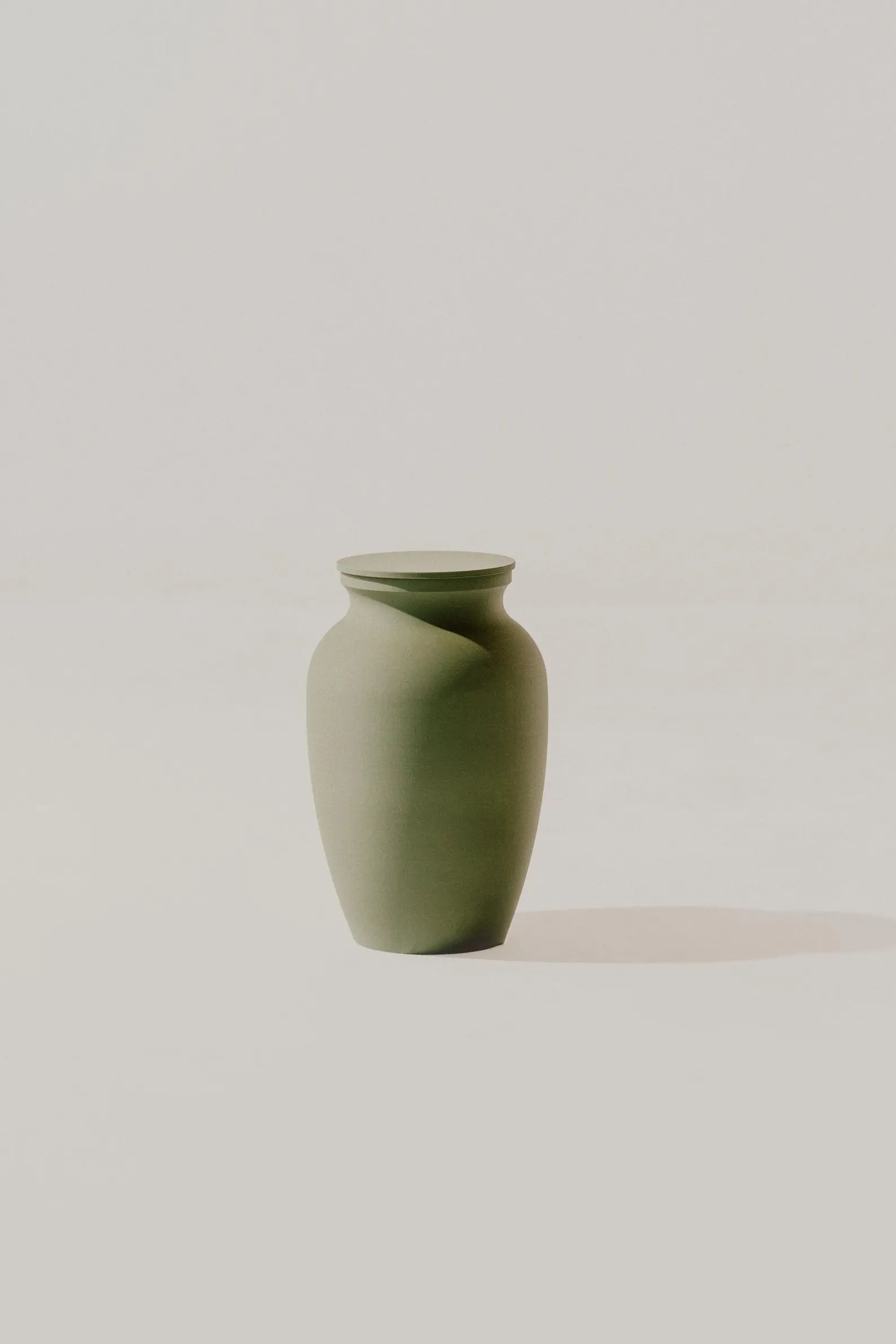 Olive smooth memorial urn on a light beige background