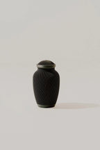 Black ribbed memorial urn on a light beige background