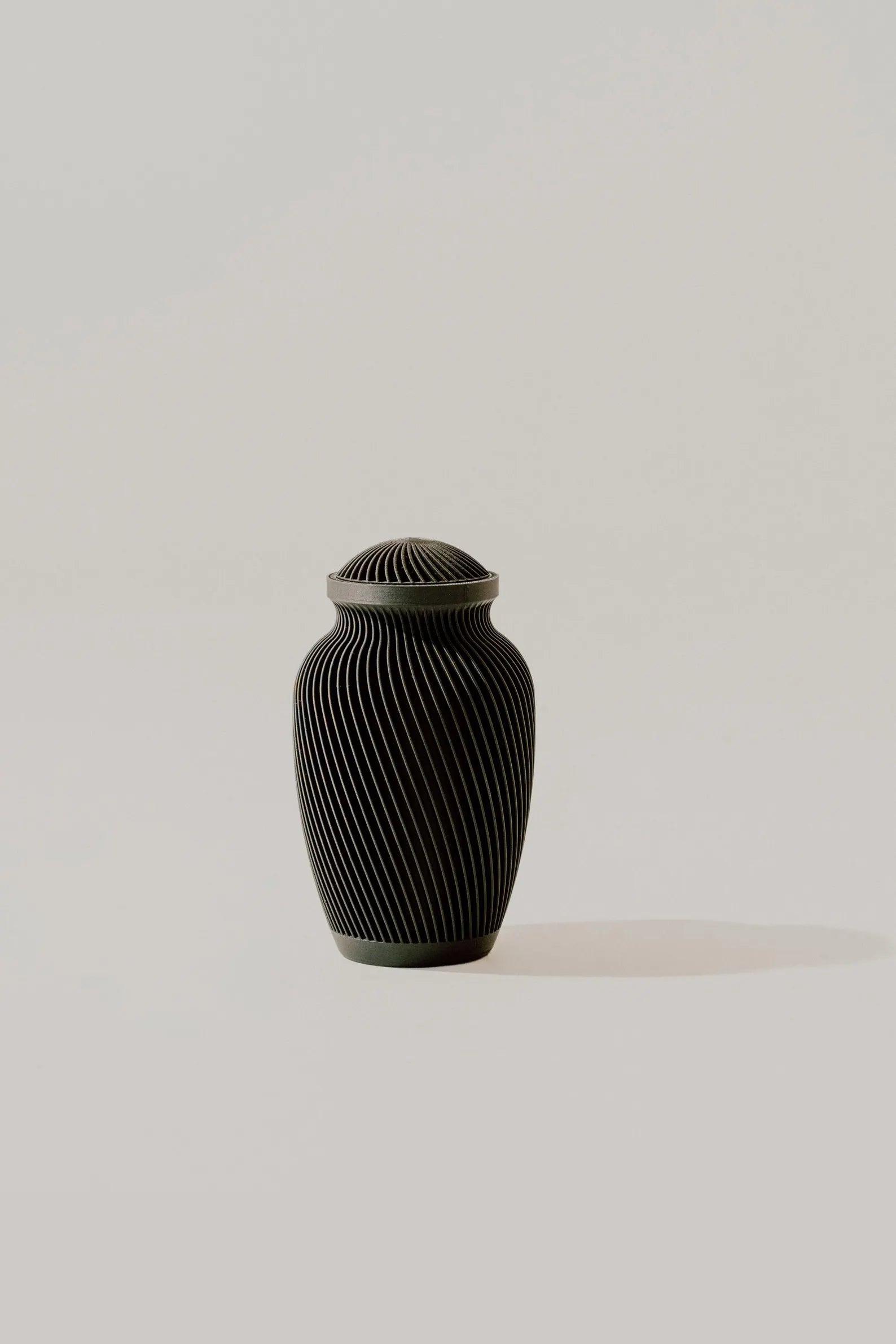 Black ribbed memorial urn on a light beige background