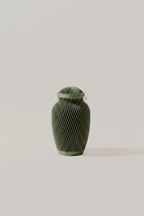 Olive green textured memorial urn on a light beige surface neutral background