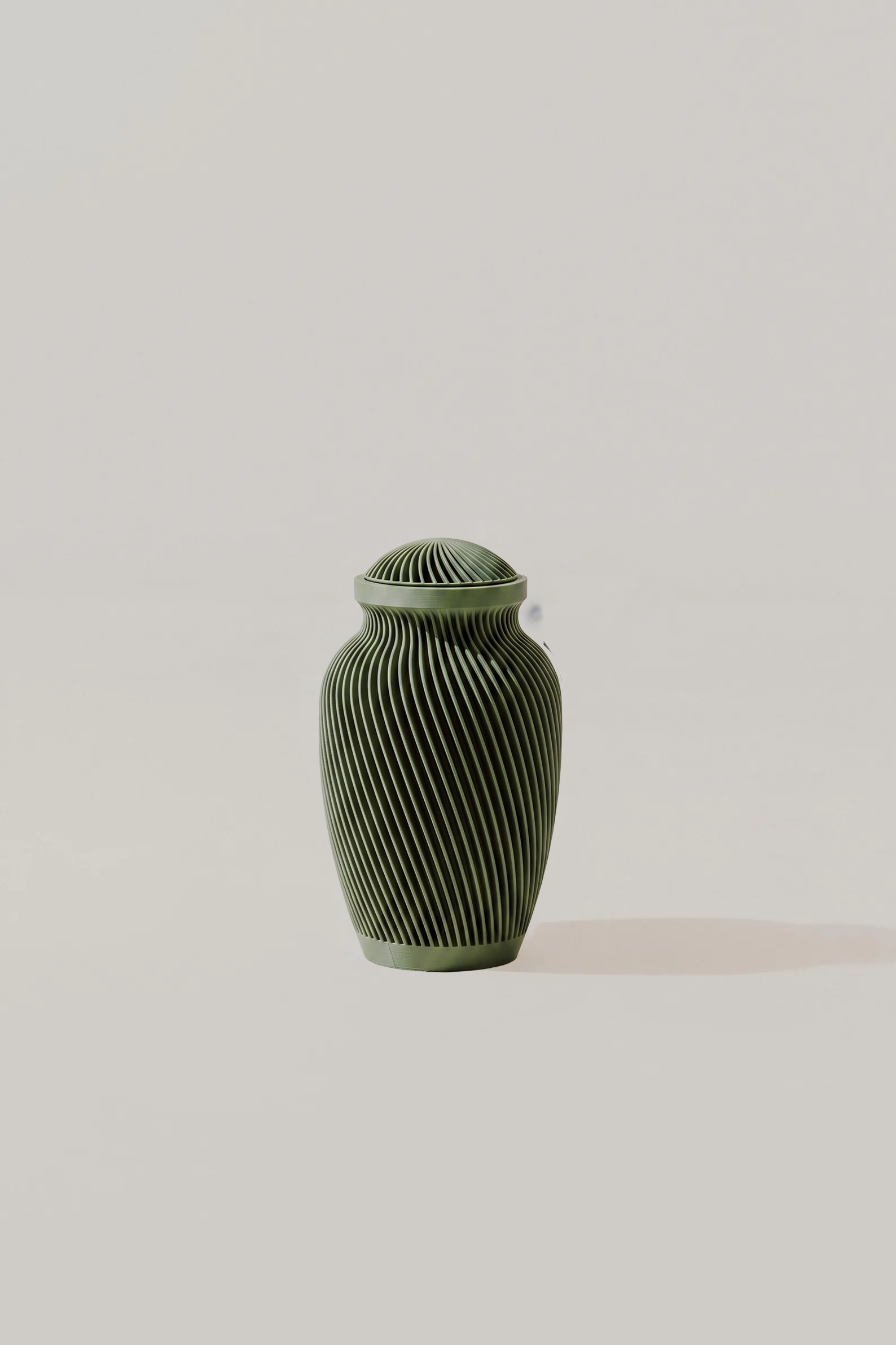 Olive green textured memorial urn on a light beige surface neutral background