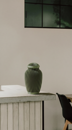 Green ribbed memorial urn on a wooden surface with a neutral background