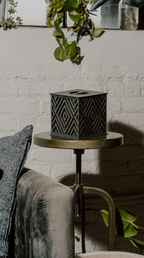Beautiful memorial urn with geometric pattern on a small round table against a white brick wall.