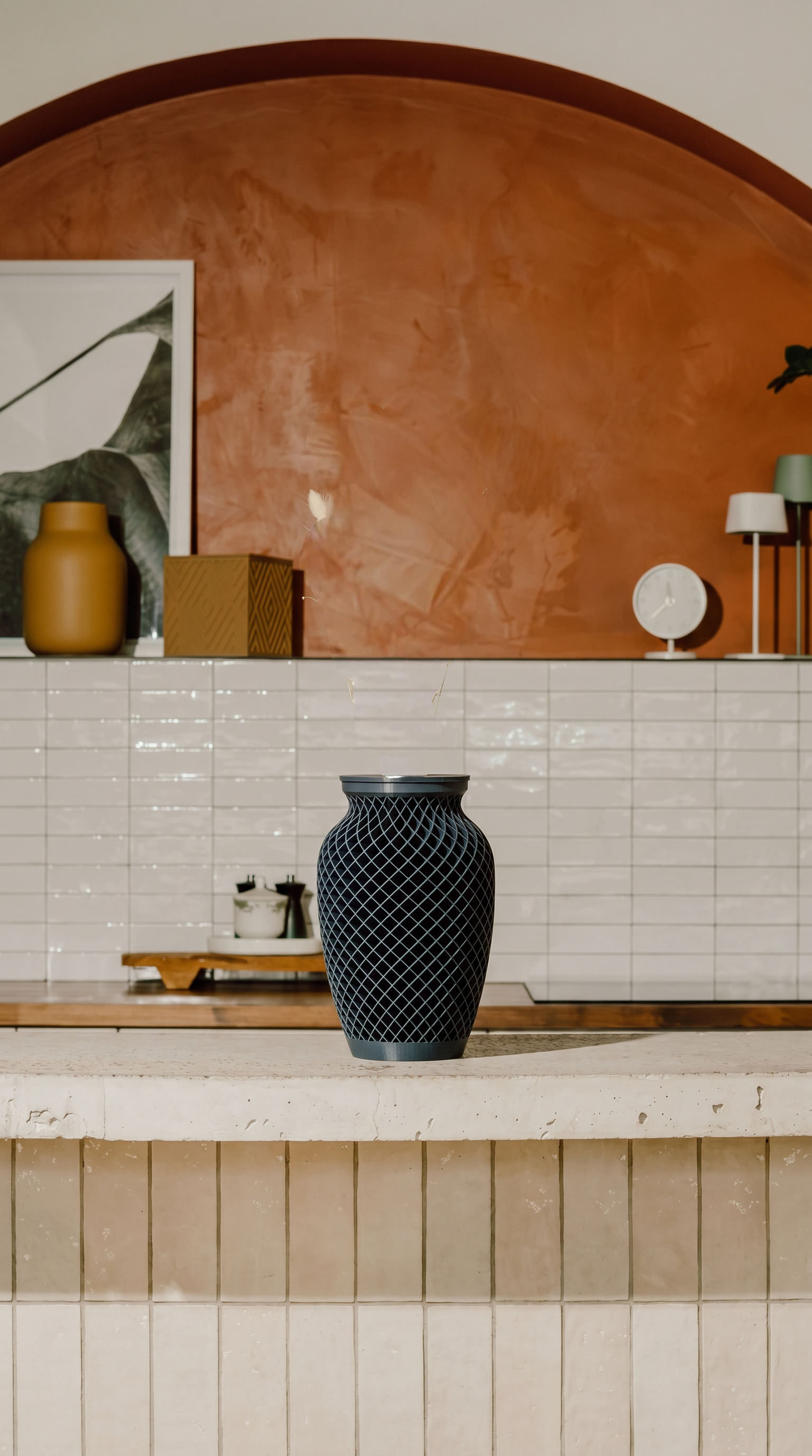 Dark blue woven texture memorial urn on a kitchen counter with a tiled wall and decorative items in the background