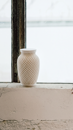 White textured memorial urn on a windowsill with a blurred outdoor background